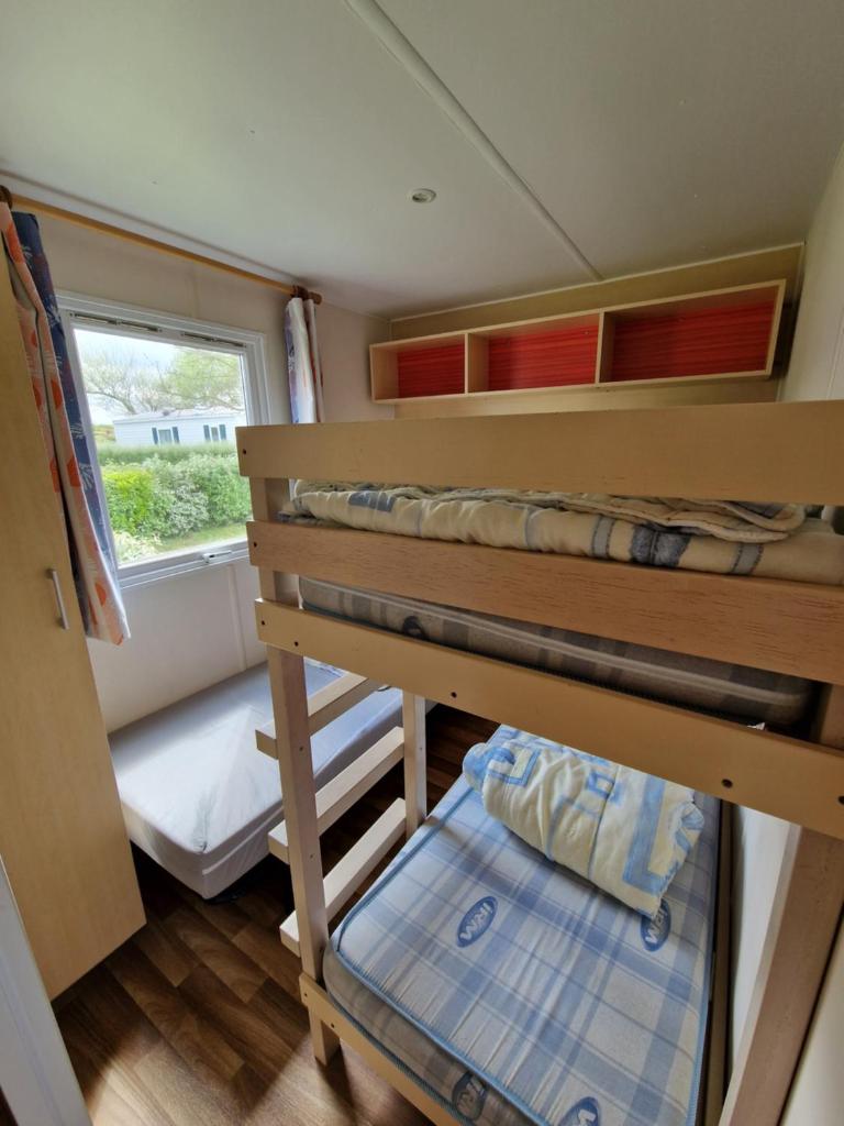 Cette petite chambre comprend des lits superposés et une fenêtre. dans l'établissement Mobil home plouescat, à Plouescat