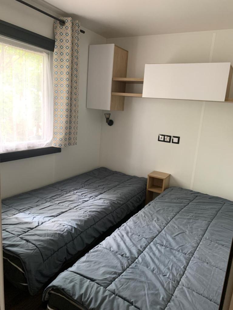 une petite chambre avec deux lits et une fenêtre dans l'établissement MH 008 Bora Bora sur emplacement exceptionnel en lisière de forêt dans camping 4 étoiles, à Saint-Julien-en-Born