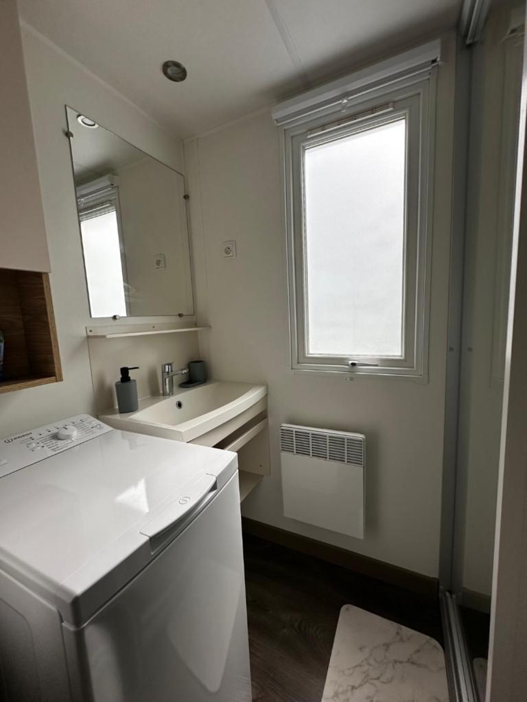 une salle de bain blanche avec un lavabo et un miroir dans l'établissement Grand Mobil Home Tout Confort pour 6 personnes - Camping Les Oyats 4 étoiles, à Seignosse