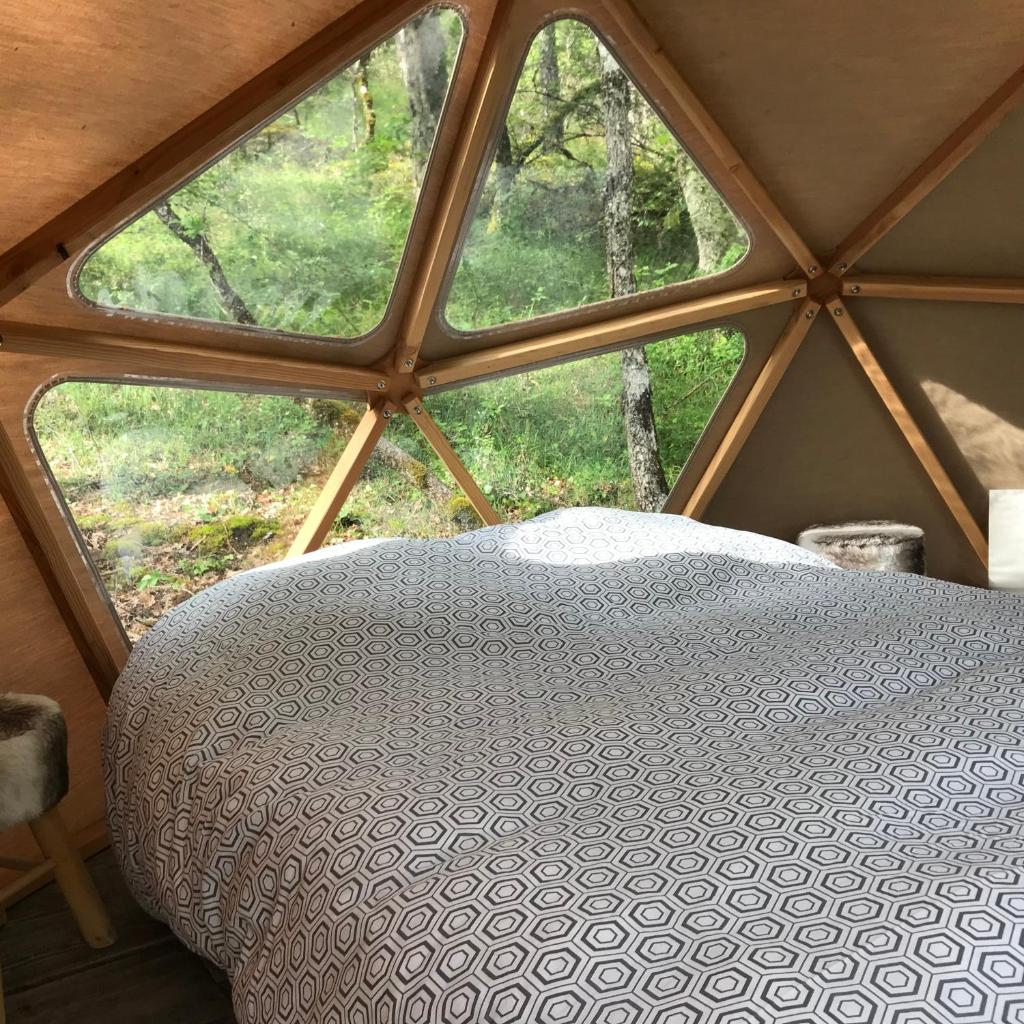 un lit dans une chambre avec une grande fenêtre dans l'établissement Arborea, nuits insolites au cœur de la forêt, à Montignac