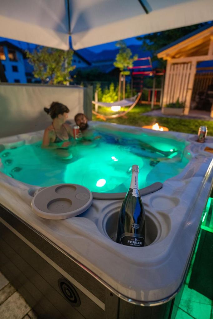 une femme dans un bain à remous avec une bouteille de vin dans l'établissement Caldonazzo Dog Sport & Wellness, à Caldonazzo