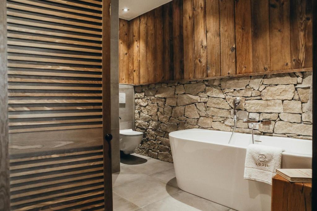 La salle de bains est pourvue d'une baignoire blanche et d'un mur en pierre. dans l'établissement Duplex Encombres by Lodji, à Saint-Martin-de-Belleville