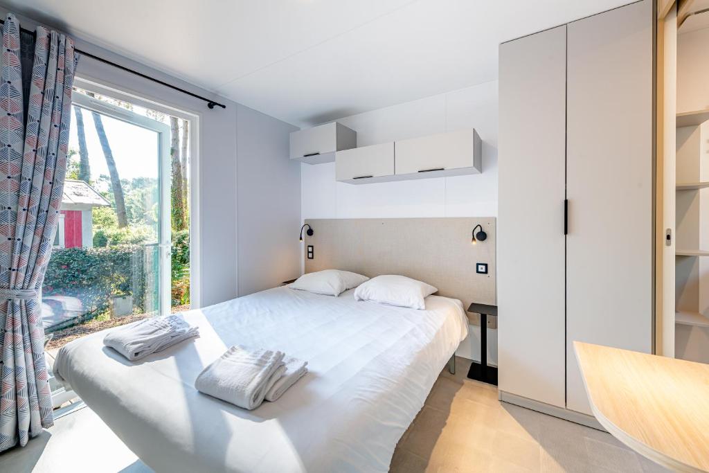 une chambre avec un lit blanc et une fenêtre dans l'établissement Camping Domaine Les Oréades - Maeva Sélection, à Sanguinet