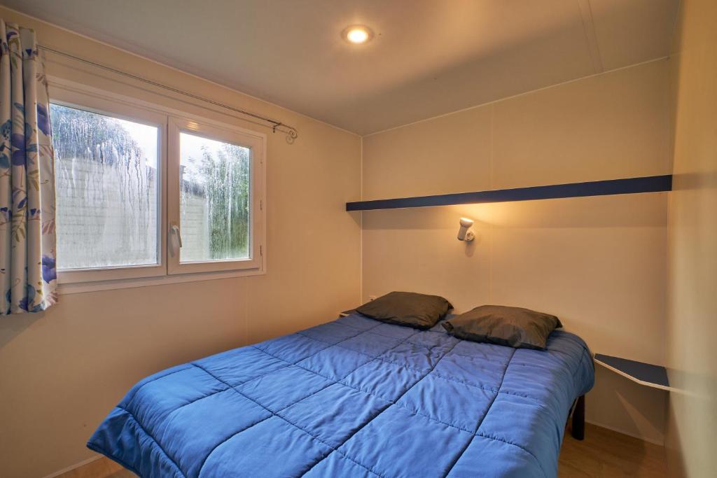 une chambre avec un lit bleu et une fenêtre dans l'établissement Mobil Home 4 personnes 202, à Mens