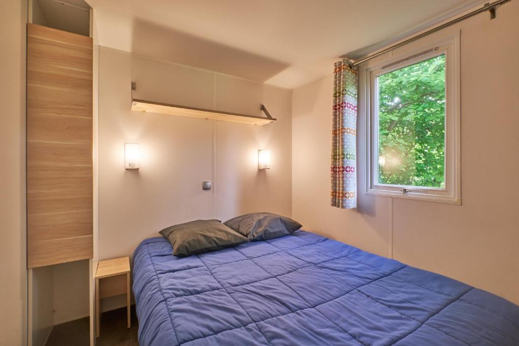 une chambre avec un lit bleu et une fenêtre dans l'établissement Mobil Home 4 personnes 204, à Mens 17 autres photos