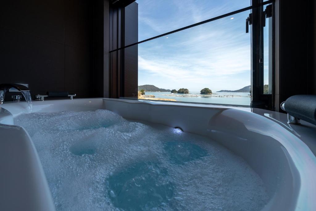 une baignoire remplie d'eau avec une grande fenêtre dans l'établissement Kochoran, à Toba