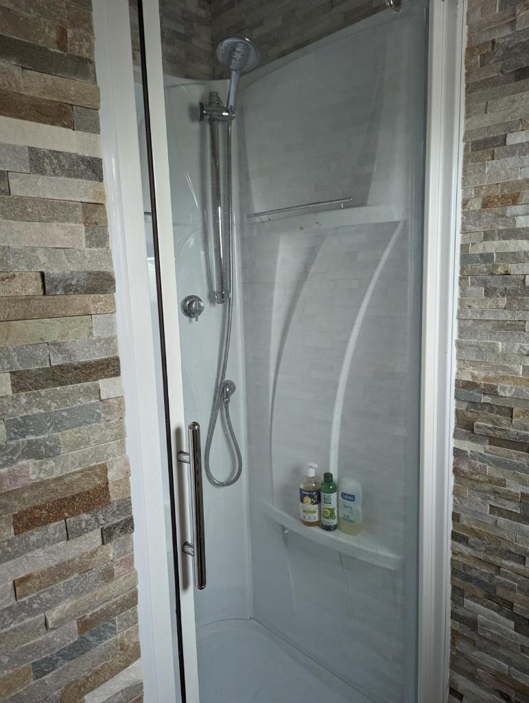 une douche avec une porte en verre à côté d'un mur de briques dans l'établissement Yourte atypique entre Lyon et Grenoble ! Vue sur les montagnes., à Nohant-en-Graçay
