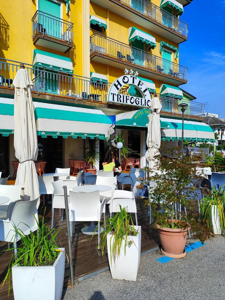 un restaurant avec des tables blanches et des parasols devant un bâtiment dans l'établissement Hotel Trifoglio, à Lido di Jesolo