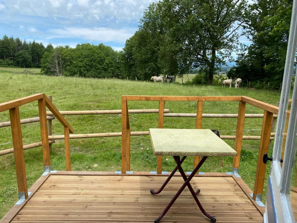 un porche en bois avec une table et un champ de vaches dans l'établissement Roulotte dans le Morvan, à Luzy