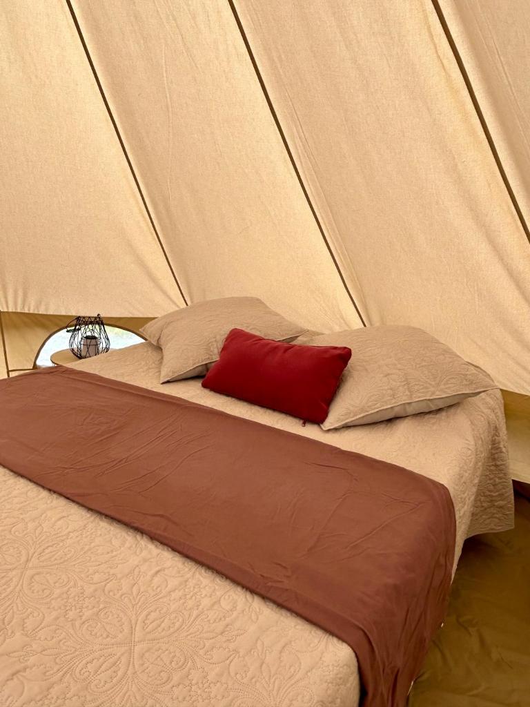 - un lit avec un oreiller rouge dans une tente dans l'établissement Chambre au jardin Tente de charme, à Éguzon-Chantôme