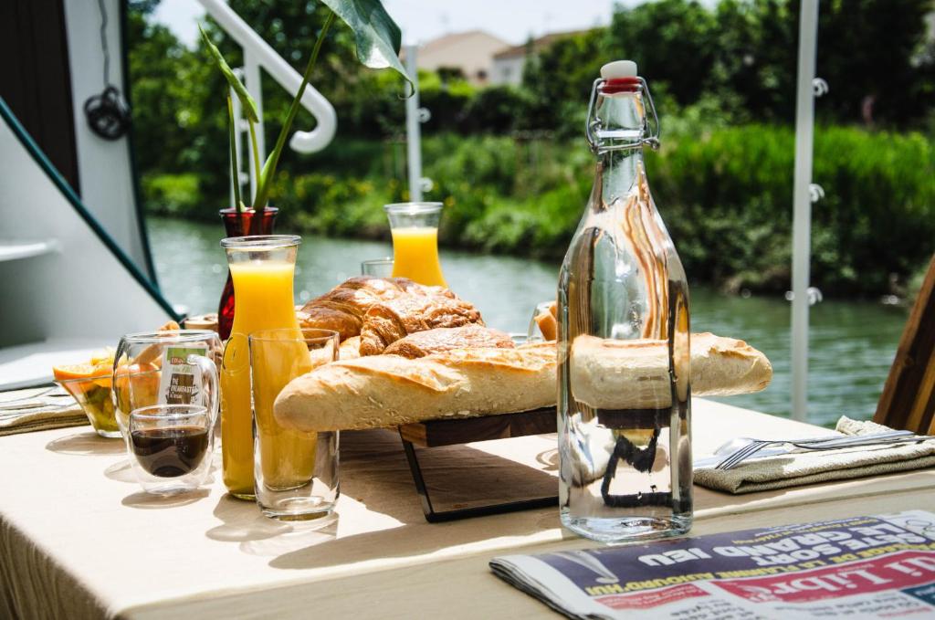- une table avec du pain et une bouteille de jus d'orange dans l'établissement Péniche La Messagère, à Villeneuve-lès-Béziers