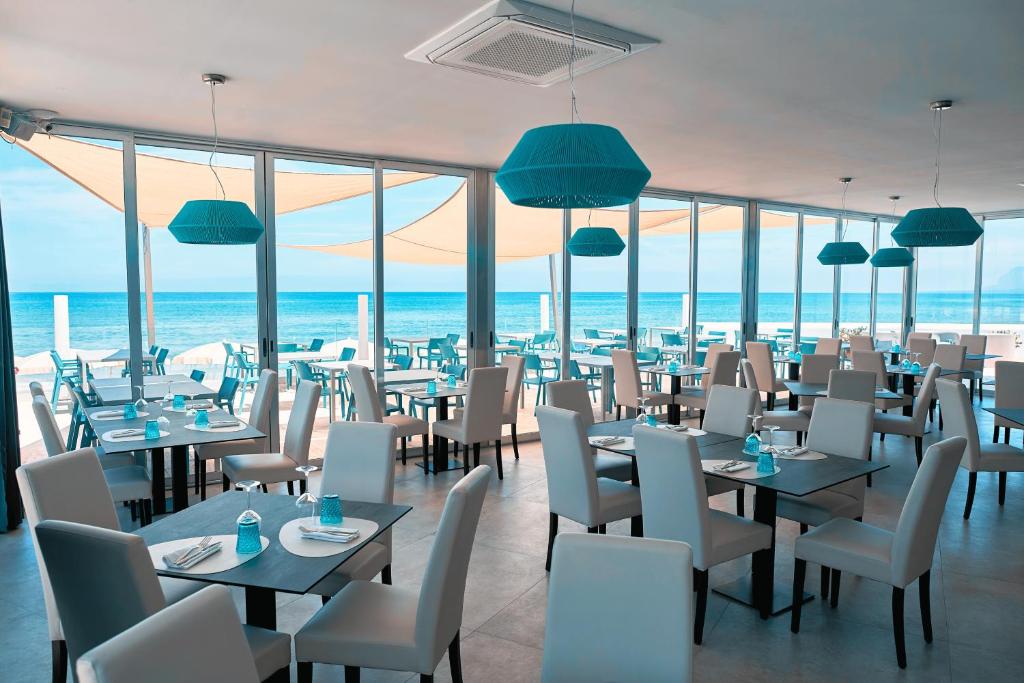 un restaurant avec des tables et des chaises avec l'océan en arrière-plan dans l'établissement Hotel La Battigia, à Alcamo Marina