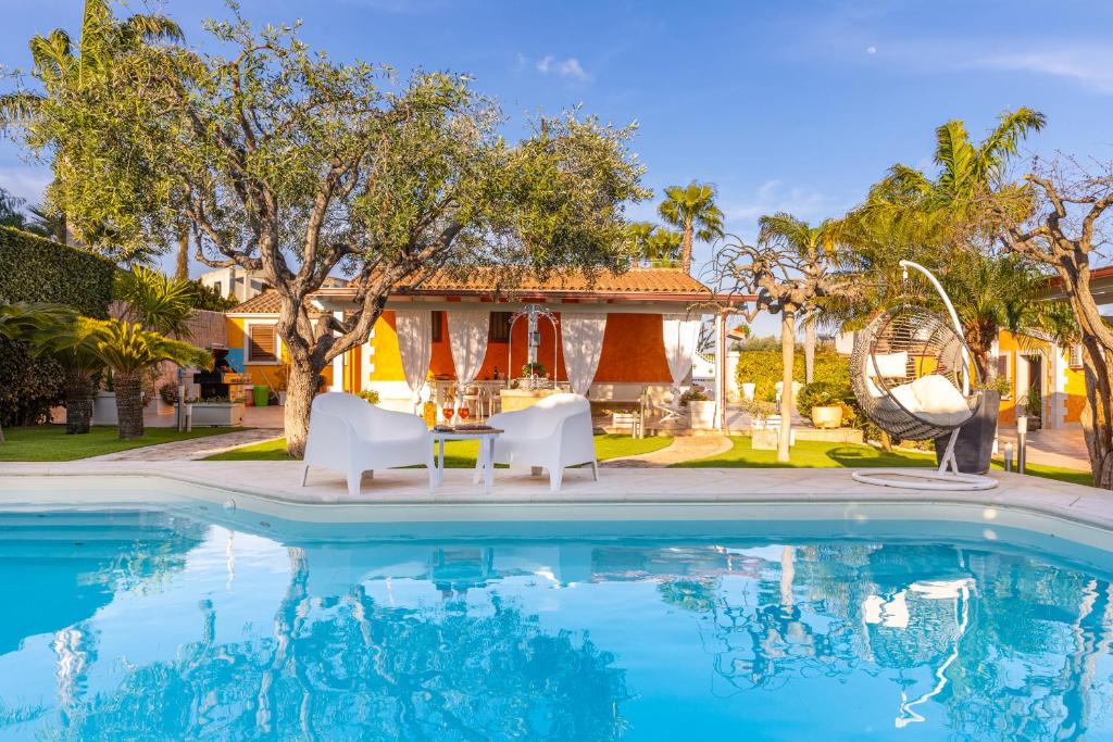 une piscine avec deux chaises blanches et une maison dans l'établissement Luxury villa at Pozzallo at 390 meters about from the beach with private swimming pool, à Pozzallo