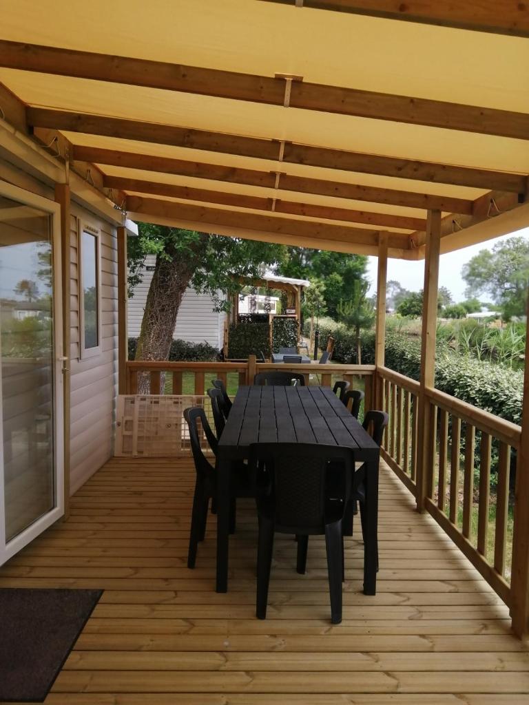 une terrasse en bois avec une table et des chaises noires dans l'établissement Mobil Home bord d'eau Camping 4 étoiles Les Viviers, à Lège-Cap-Ferret