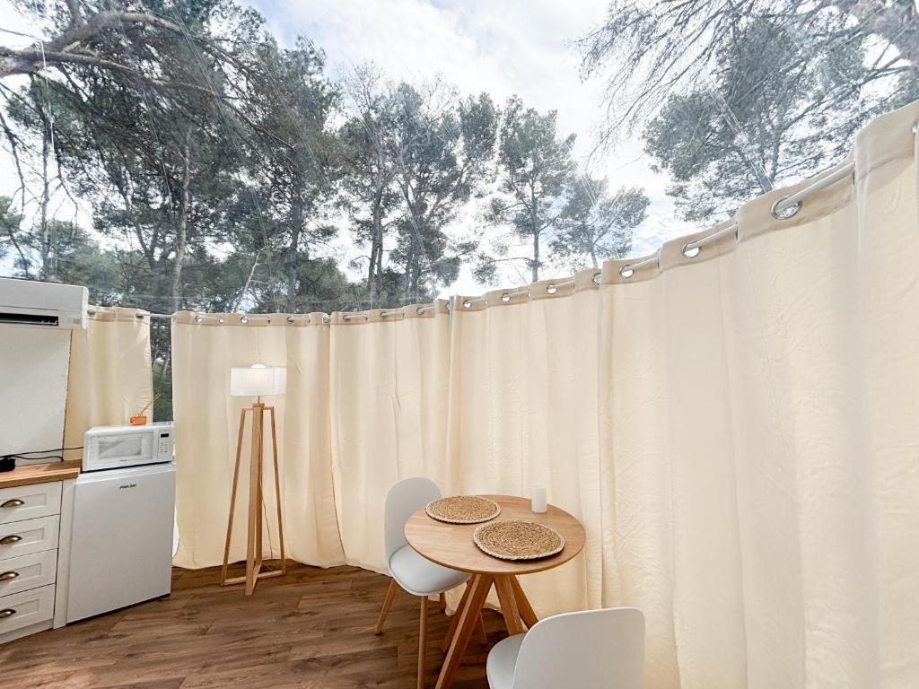 une cuisine avec des rideaux blancs et une table avec des chaises dans l'établissement La Bulle des Pins, à Istres