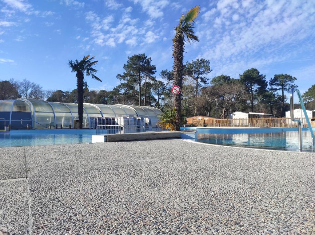 une piscine avec des palmiers et un bâtiment dans l'établissement lesmobilhomesduferret - camping Les Viviers - mobil-homes de particuliers, funpass activités non inclus, à Lège-Cap-Ferret