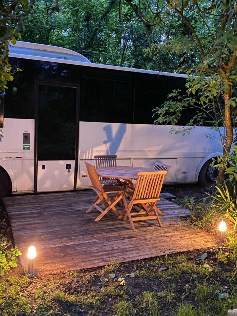 une terrasse en bois avec une table et deux chaises et un bus dans l'établissement Woody Wood Bus, à Vergeroux 5 autres photos