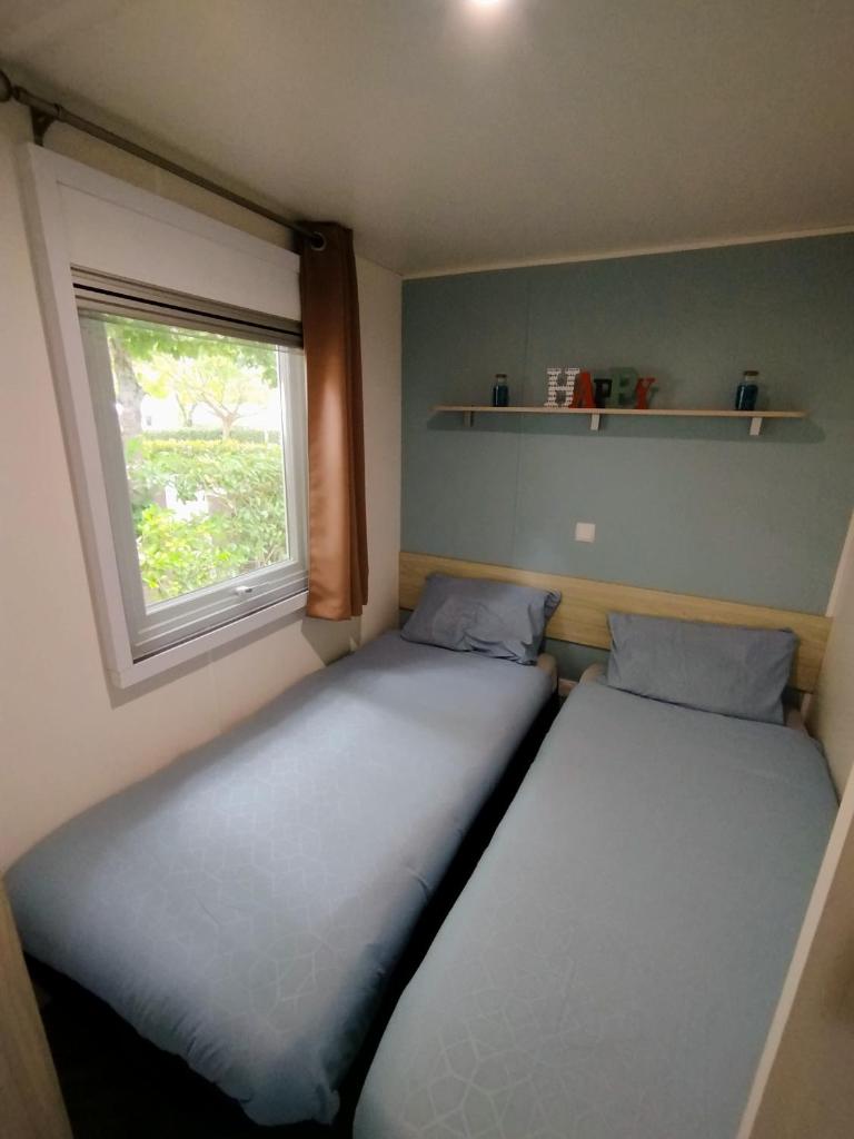 deux lits dans une petite pièce avec une fenêtre dans l'établissement Mobil-home, à Gastes