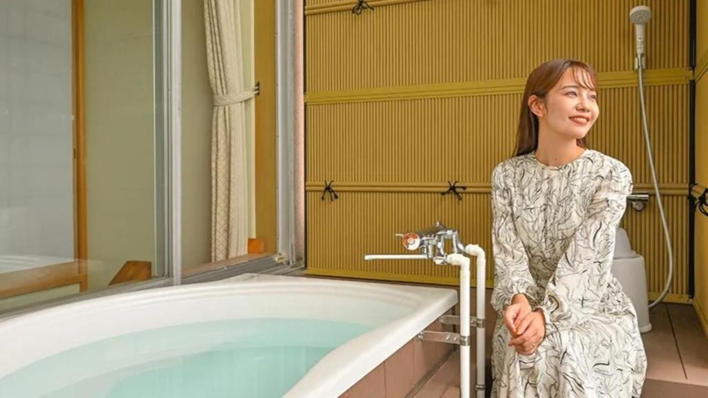 une femme debout à côté d'une baignoire dans une salle de bains dans l'établissement Futagojimasou, à Wakayama