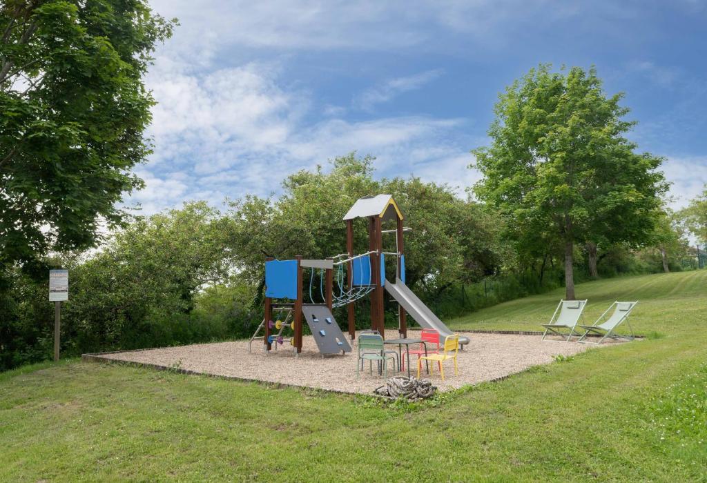 une aire de jeux avec un toboggan et des chaises dans un parc dans l'établissement Camping Le Mont Libre - Cottage & espace nature - Gannat, à Gannat