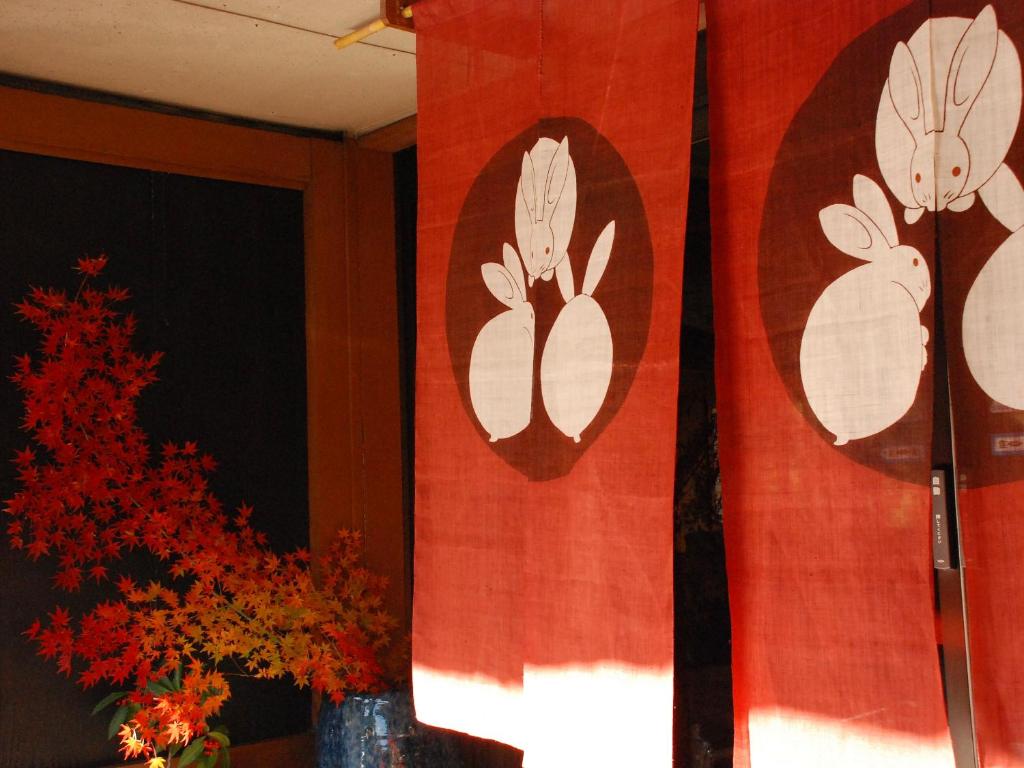 un rideau rouge avec des fleurs blanches sur un mur dans l'établissement Sakaya Ryokan Yoshina Onsen, à Izu