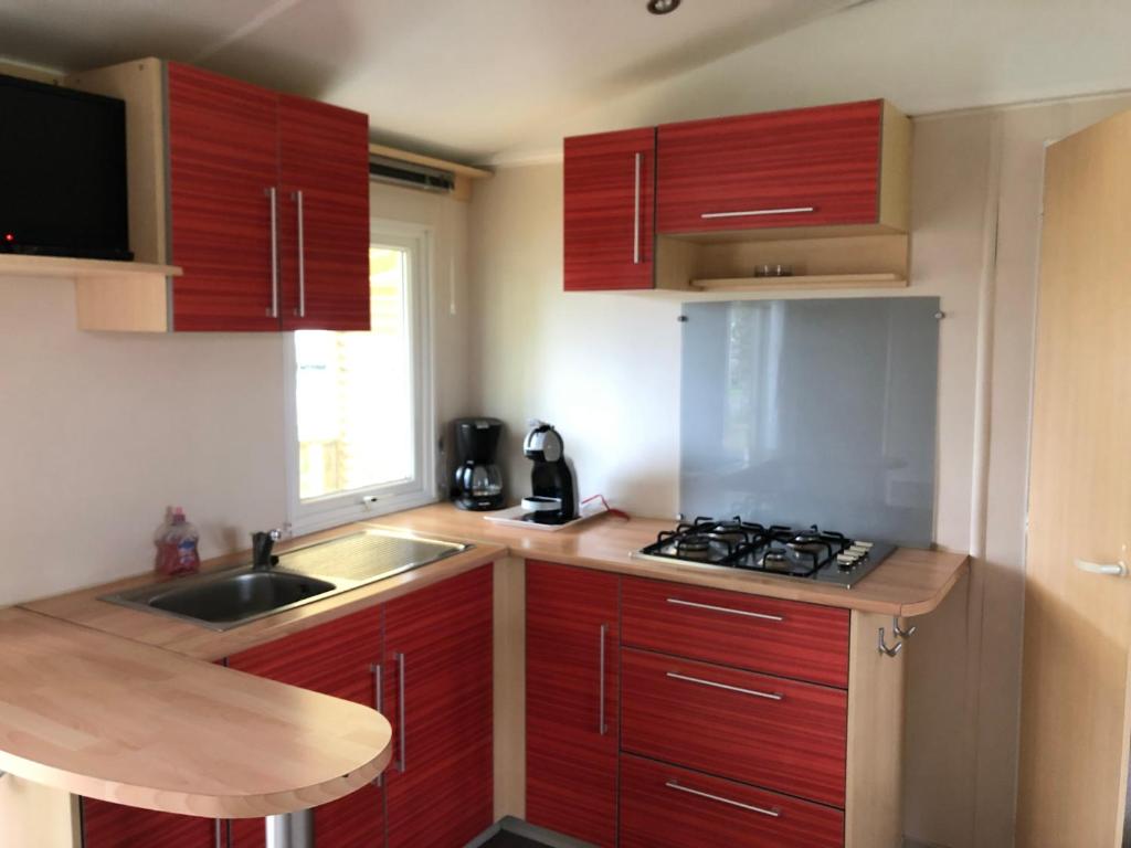 une petite cuisine avec des armoires rouges et un évier dans l'établissement Bungalow "CONFORT" PUY duFOU 2CH-5pers 720FA, à La Boissière-de-Montaigu 2 autres photos
