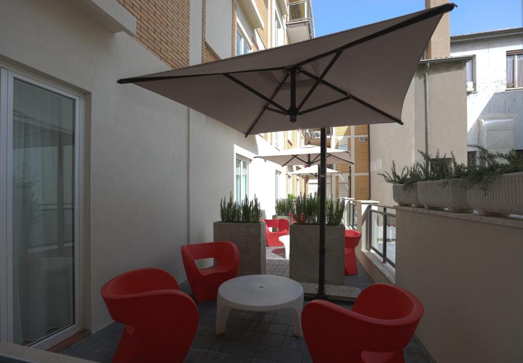 une terrasse avec des chaises rouges, une table et un parasol dans l'établissement DuoMo Hotel, à Rimini