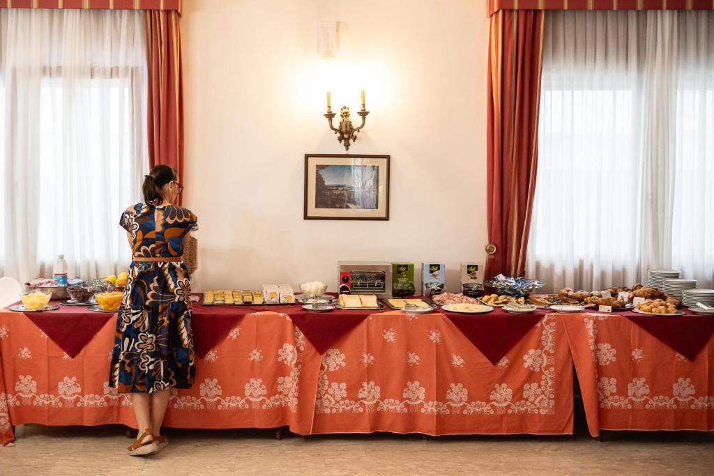une femme debout devant une table avec de la nourriture dans l'établissement Easy Hotel Meryon, à Sottomarina
