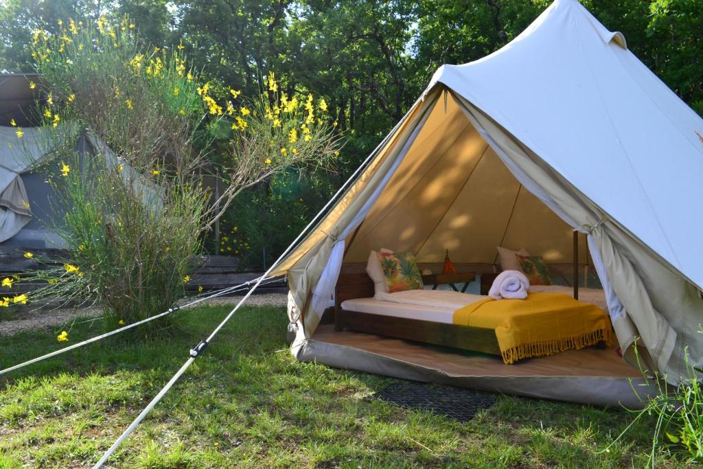 une tente blanche avec un lit dans l'herbe dans l'établissement Le Camp, à Varen