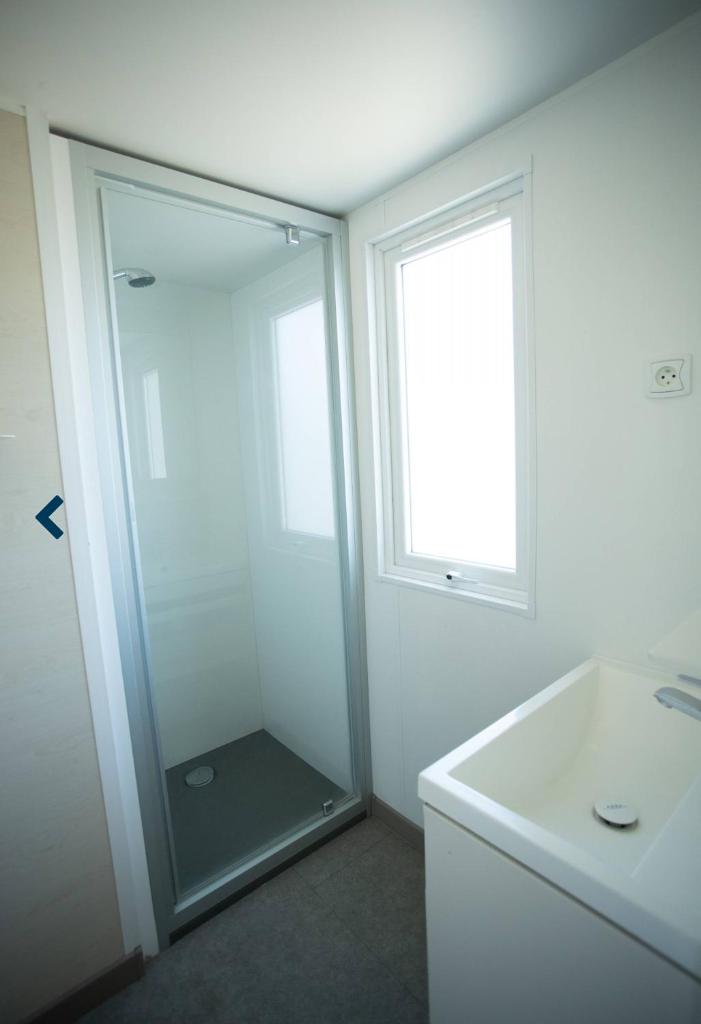 une salle de bain blanche avec une douche et un lavabo dans l'établissement Mobilhome dans camping 4 étoiles, au Cap d'Agde