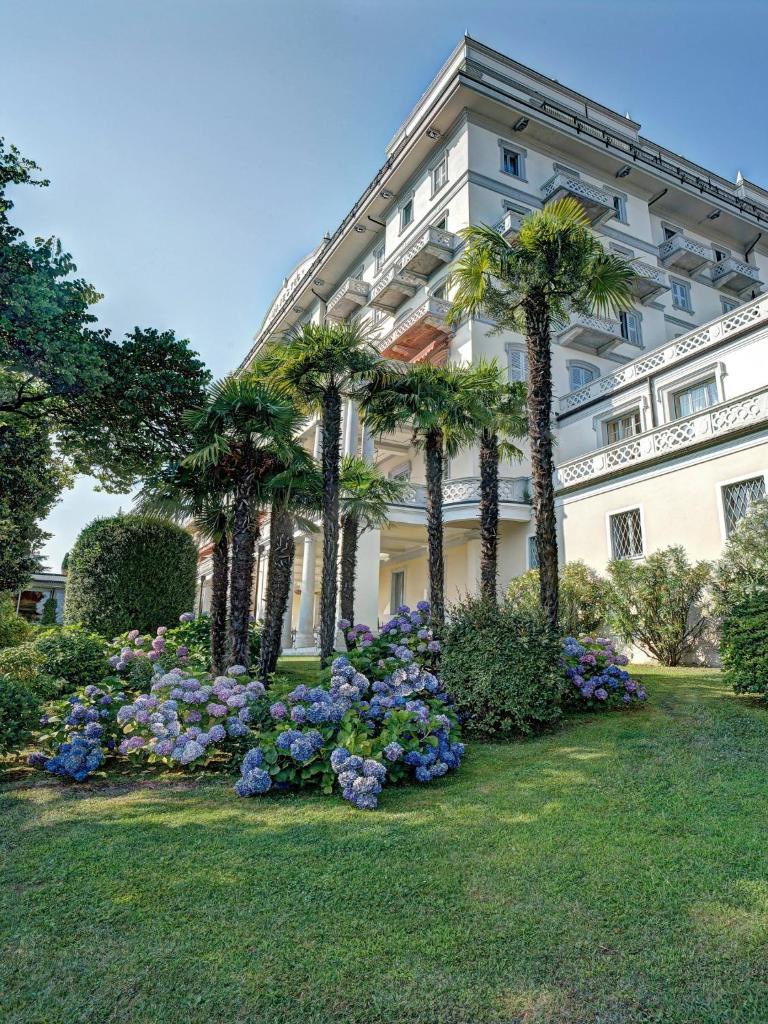 un bâtiment avec des palmiers et des fleurs devant lui dans l'établissement Grand Hotel Majestic, à Verbania