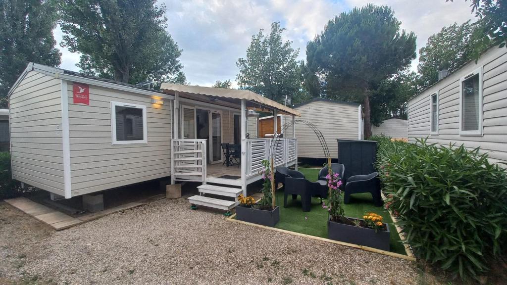 Une petite maison blanche avec une terrasse couverte et quelques plantes dans l'établissement Mobil home à Vias - Vos vacances à la mer, à Vias