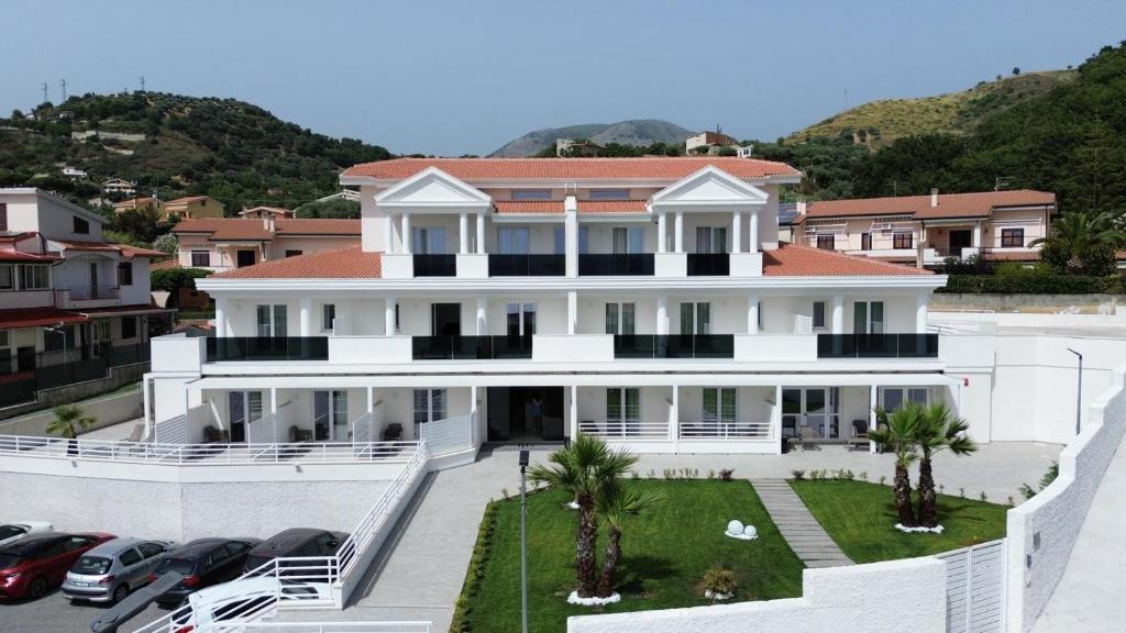 une grande maison blanche avec des voitures garées sur un parking dans l'établissement Hotel Diadema, à Diamante