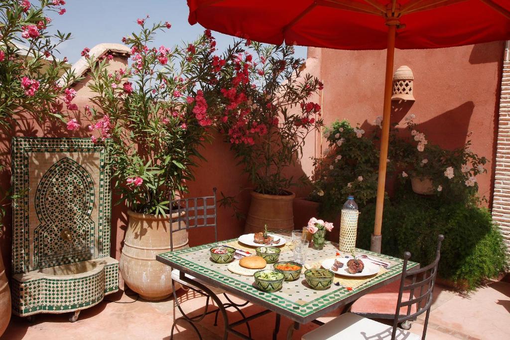 une table avec des assiettes de nourriture et un parapluie rouge dans l'établissement Riad Chameau FDC Hôtel SPA, à Marrakech