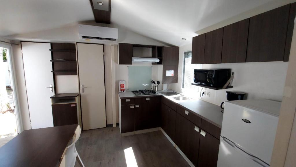 Elle comprend une petite cuisine avec des placards bruns et un four micro-ondes. dans l'établissement camping marvilla les 7 fonds, à Agde