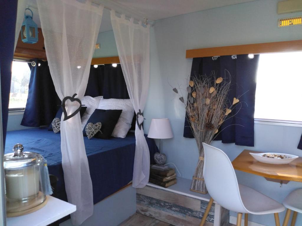une chambre avec un lit bleu avec des rideaux et une table dans l'établissement Caravane Seventies avec jacuzzi, à Lapalisse