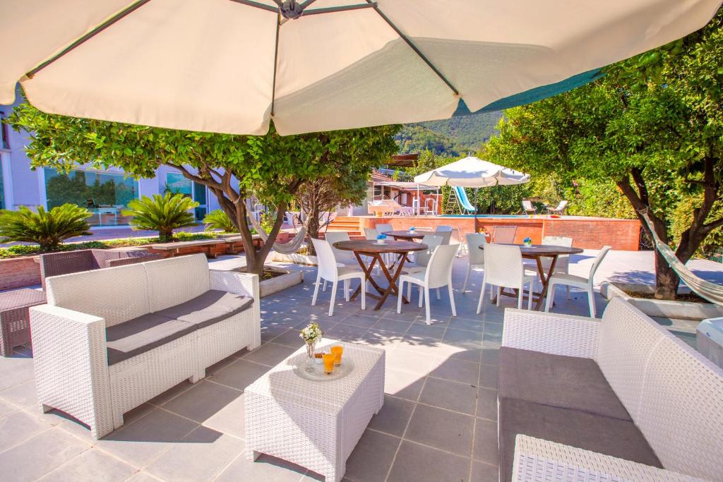 un patio extérieur avec tables, chaises et un parasol dans l'établissement Villa Amore seaview pool garden & SPA, à Castellammare di Stabia