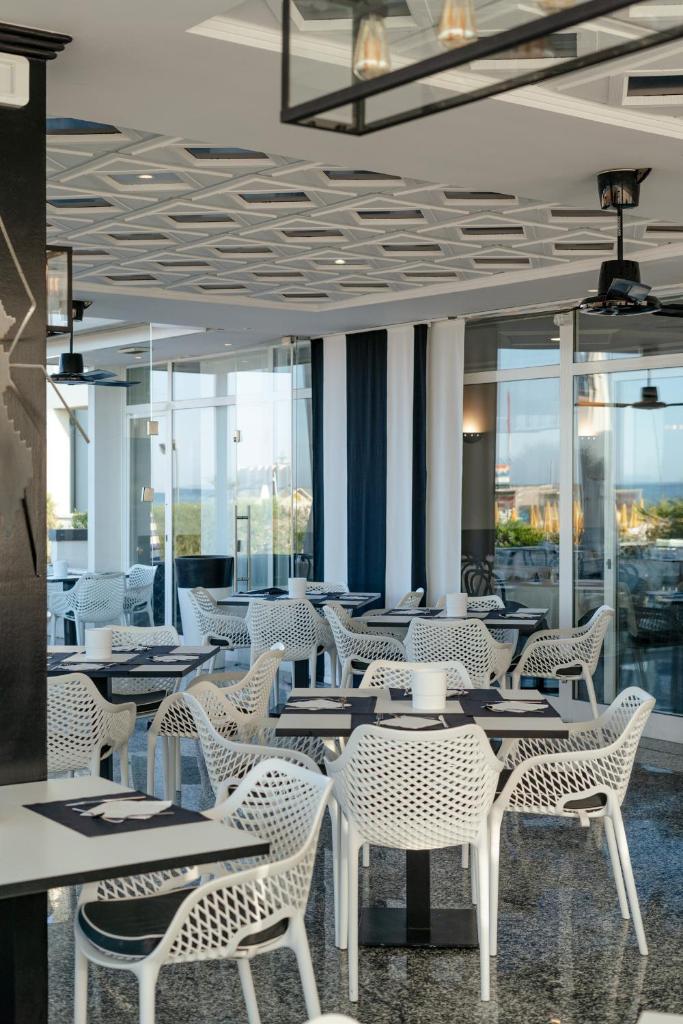 un restaurant avec des chaises et des tables blanches et des fenêtres dans l'établissement Hotel Gritti, à Lido di Jesolo