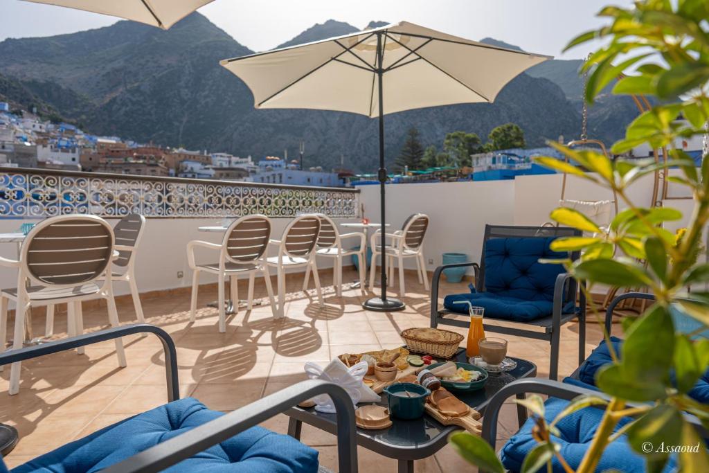 une terrasse avec des chaises, des tables et un parasol dans l'établissement Dar Kisania, à Chefchaouen