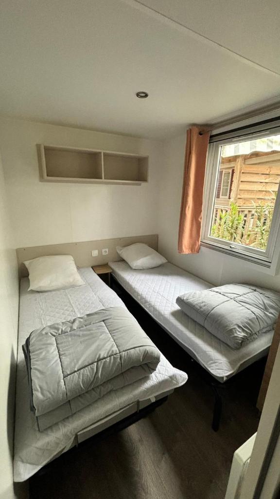 deux lits dans une chambre avec une fenêtre dans l'établissement MH T003 3 chambres 38m2 année juin 2021 Clim TV lave vaisselle dans camping 4 étoiles, à Saint-Julien-en-Born