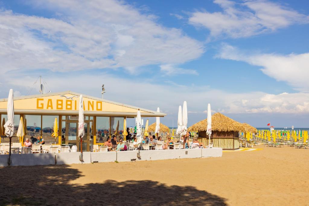 - un bâtiment sur une plage avec des chaises et des parasols dans l'établissement Aparthotel Carinzia, à Lignano Sabbiadoro