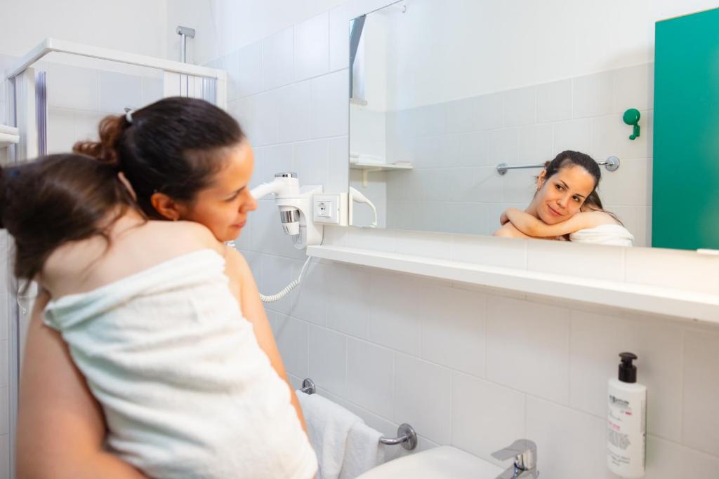 une femme regardant son reflet dans un miroir de salle de bain dans l'établissement Aparthotel Carinzia, à Lignano Sabbiadoro