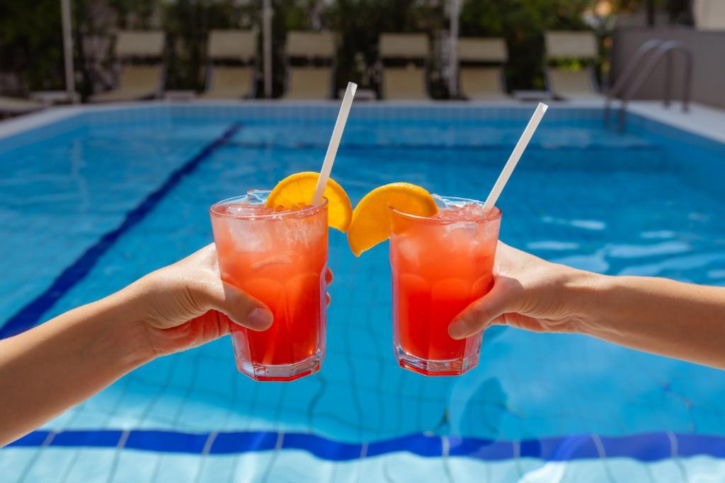 une personne tenant deux boissons dans ses mains près d'une piscine dans l'établissement Aparthotel Carinzia, à Lignano Sabbiadoro