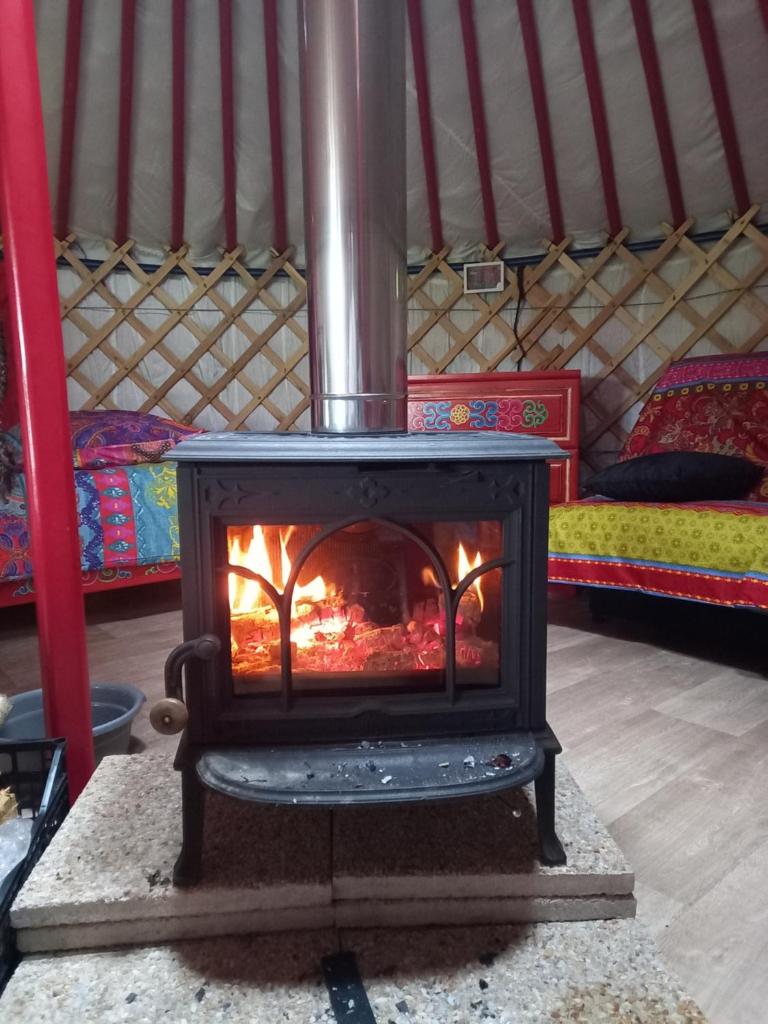 un poêle dans une yourte avec un lit dans l'établissement Yourte calvados, à Les Moutiers-en-Auge