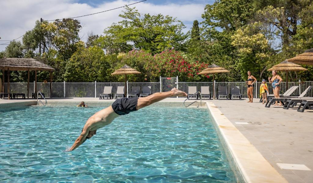 un homme plonge dans une piscine dans l'établissement Camping maeva Escapades Le Hameau des Pins, à La Crau