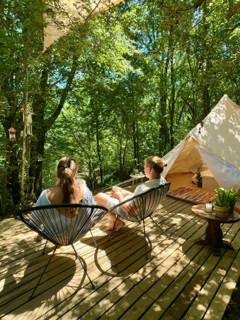 deux femmes assises sur des chaises sur une terrasse avec une tente dans l'établissement Wild Lodge, à Lasséran