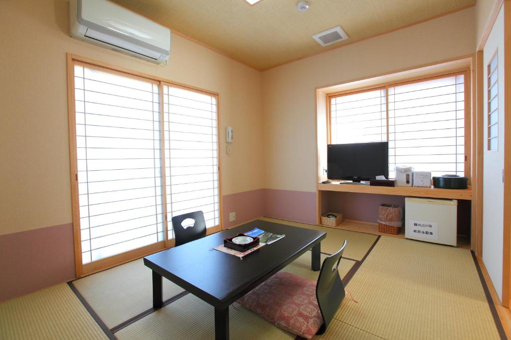 un salon avec une table, des chaises et des fenêtres dans l'établissement 和みの宿 弓ヶ浜いち番館, à Minamiizu