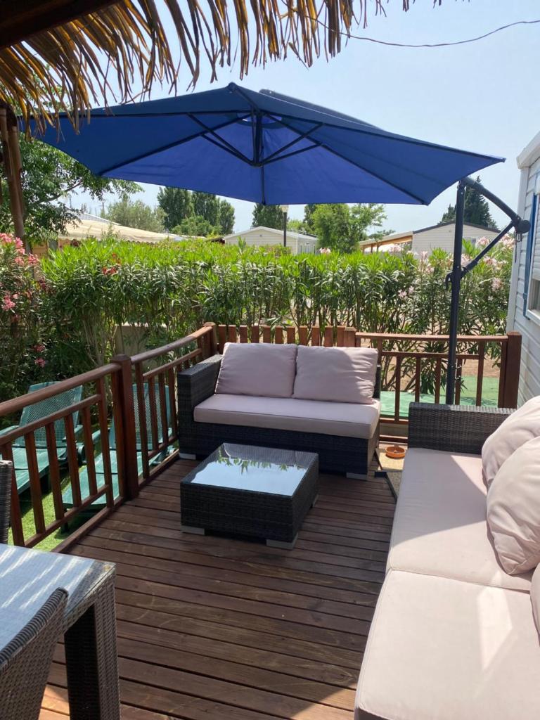 une terrasse avec un canapé et un parasol bleu dans l'établissement Mobil Home dans le camping 4 étoiles le Montourey, à Fréjus