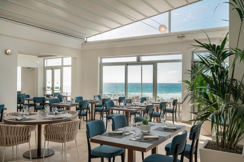 un restaurant avec des tables et des chaises avec l'océan en arrière-plan dans l'établissement Bellevue Sardinia Resort Affiliated by Meliá, à Valledoria