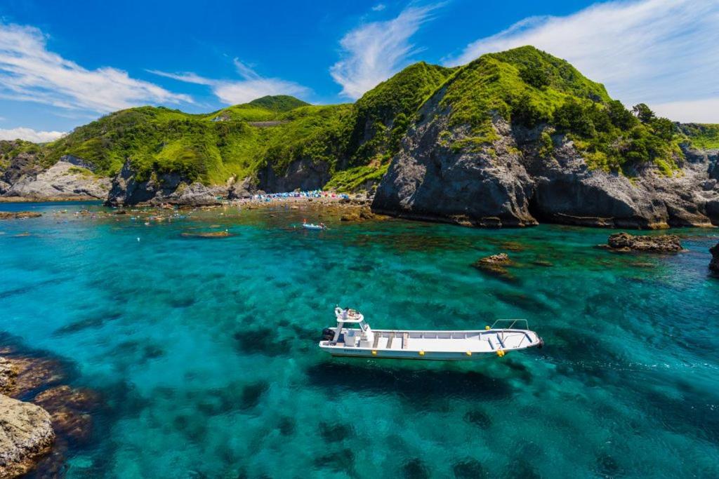 un bateau dans l'eau à côté d'une montagne dans l'établissement 和みの宿 弓ヶ浜いち番館, à Minamiizu